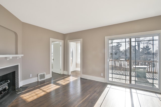 unfurnished living room featuring a brick fireplace and dark wood-type flooring