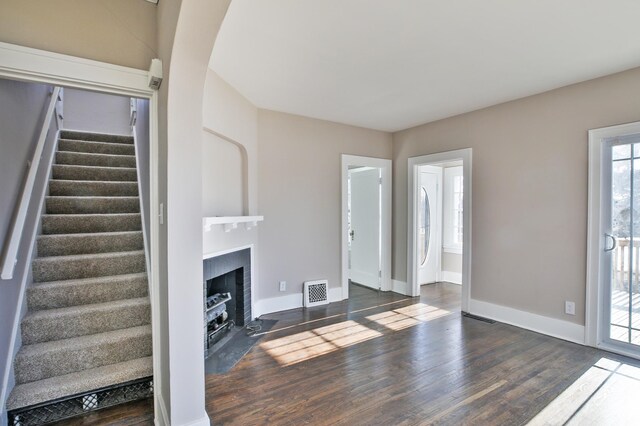 unfurnished living room with visible vents, a fireplace with flush hearth, wood finished floors, baseboards, and stairs
