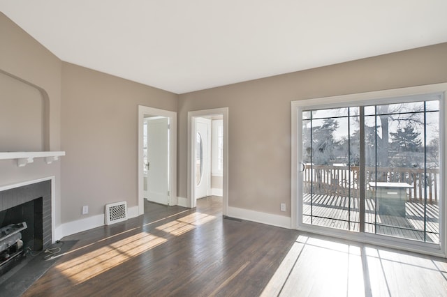 unfurnished living room with a brick fireplace, wood finished floors, visible vents, and baseboards