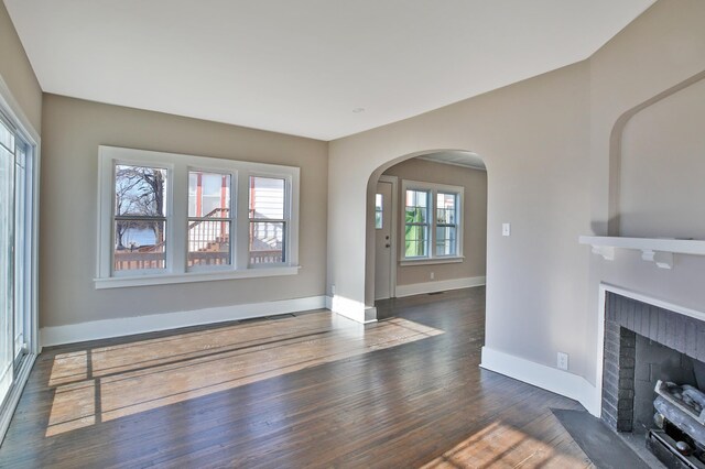 unfurnished living room with arched walkways, a fireplace, baseboards, and wood finished floors