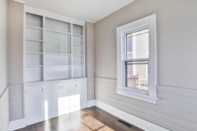 spare room with dark wood-style flooring, visible vents, plenty of natural light, and wooden walls