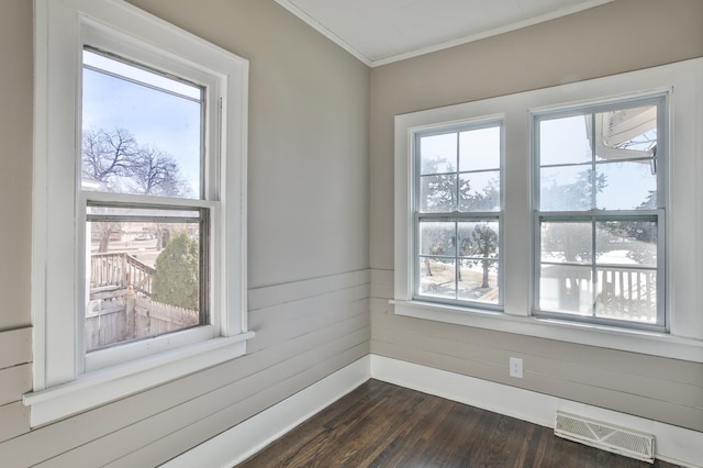 empty room with crown molding, visible vents, dark wood finished floors, and a wealth of natural light