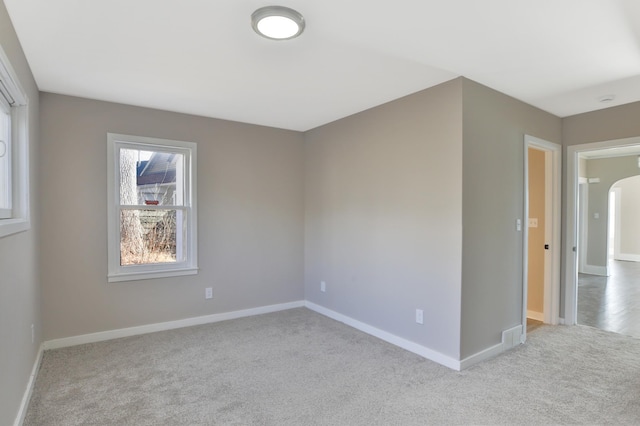 spare room with carpet floors, arched walkways, and baseboards