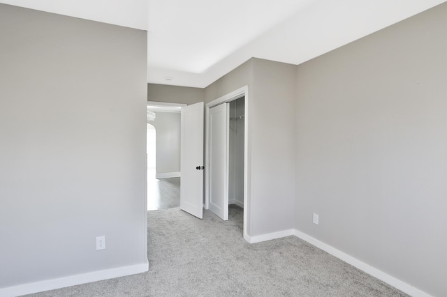 unfurnished bedroom featuring arched walkways, a closet, carpet, and baseboards