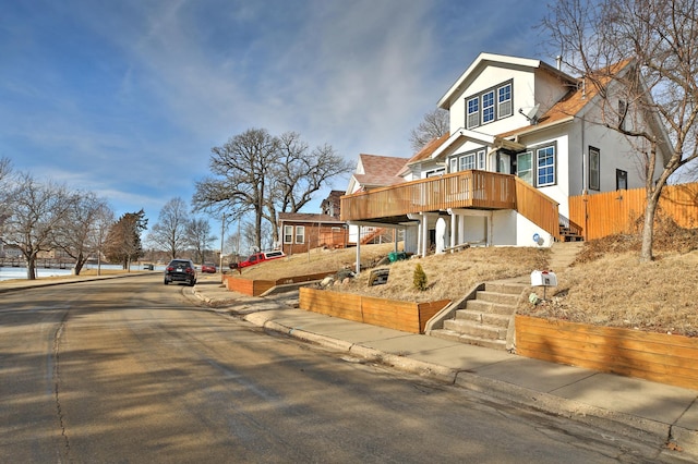 view of front facade featuring stairway, fence, a wooden deck, and stucco siding