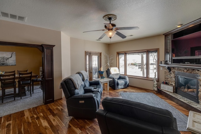 living room featuring ceiling fan, dark hardwood / wood-style floors, a textured ceiling, and a fireplace