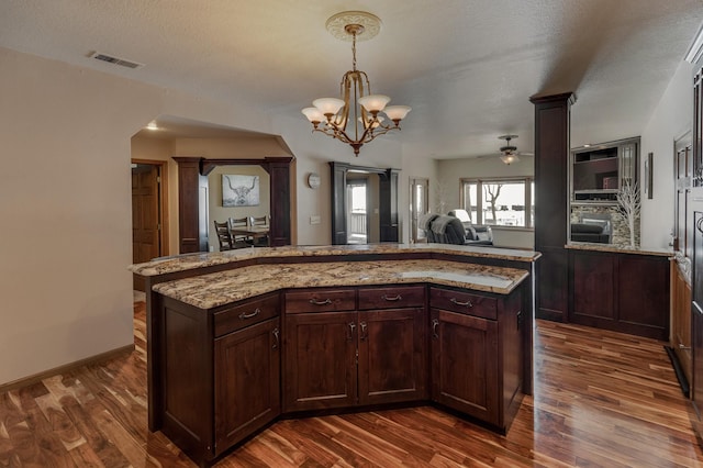 kitchen featuring dark brown cabinetry, decorative light fixtures, a center island, dark hardwood / wood-style flooring, and light stone countertops