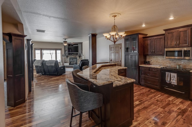 kitchen featuring a breakfast bar, black electric range oven, light stone counters, decorative light fixtures, and dark hardwood / wood-style floors