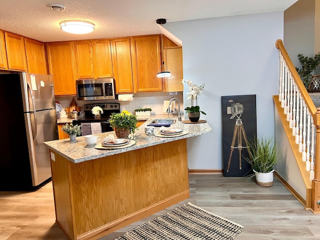 kitchen featuring appliances with stainless steel finishes, sink, light stone counters, light hardwood / wood-style floors, and kitchen peninsula