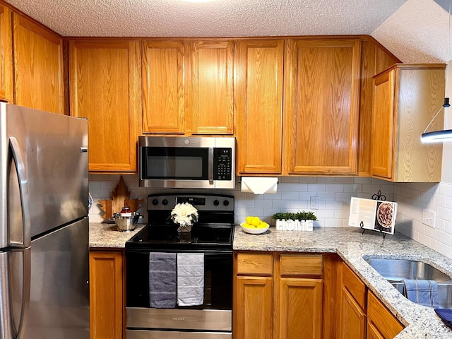 kitchen featuring a textured ceiling, backsplash, light stone countertops, and stainless steel appliances