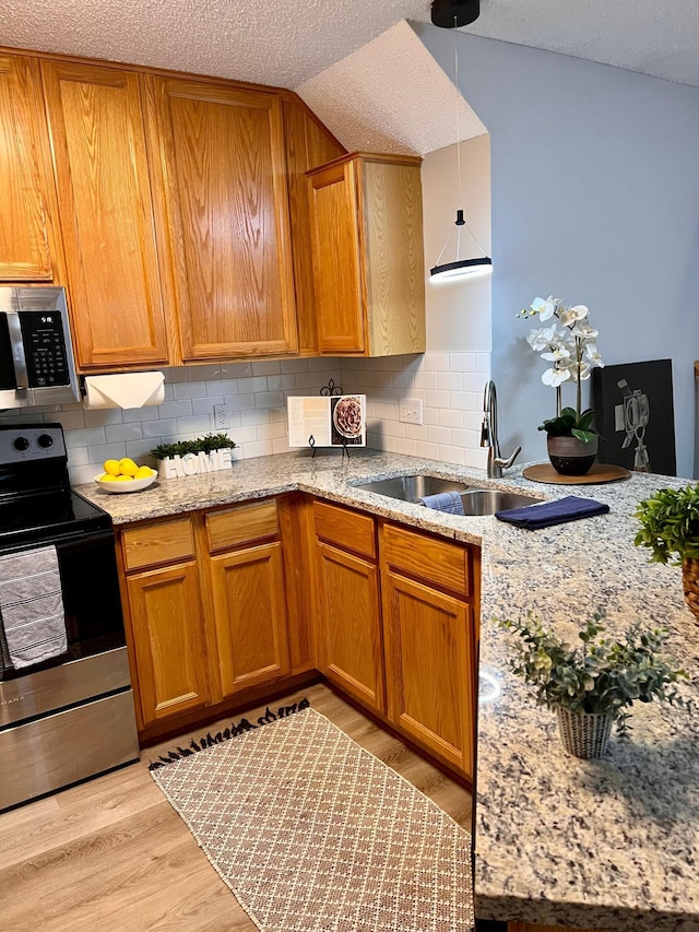 kitchen featuring appliances with stainless steel finishes, light wood-type flooring, a textured ceiling, backsplash, and sink