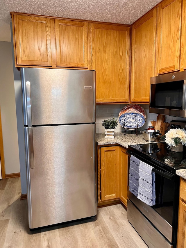 kitchen featuring light wood-type flooring, stainless steel appliances, light stone counters, and a textured ceiling