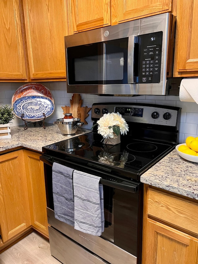 kitchen with appliances with stainless steel finishes, light stone counters, and backsplash