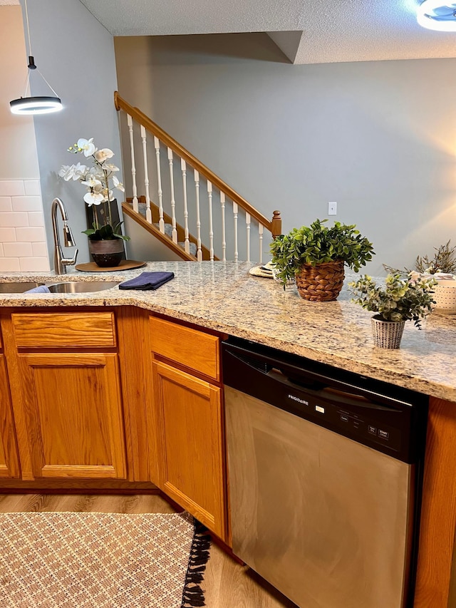 kitchen with sink, light wood-type flooring, dishwasher, hanging light fixtures, and light stone countertops