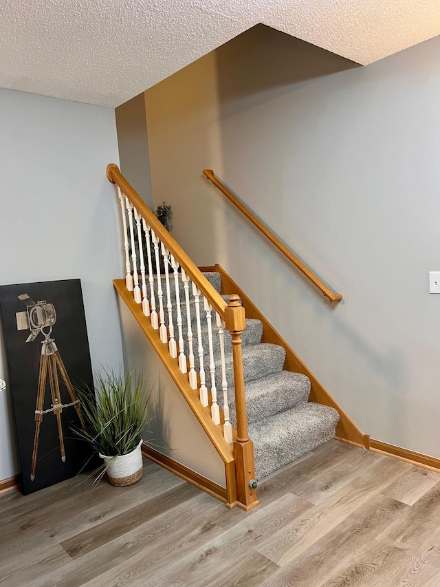 stairway with wood-type flooring and a textured ceiling