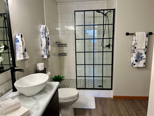 bathroom featuring toilet, tiled shower, vanity, and hardwood / wood-style flooring