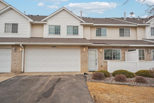 multi unit property featuring driveway, a shingled roof, an attached garage, and brick siding