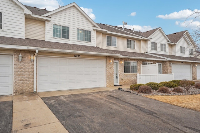 multi unit property with a garage, brick siding, roof with shingles, and aphalt driveway