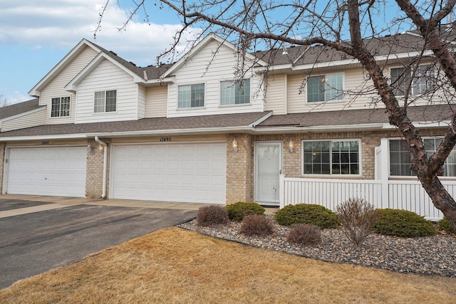 view of property featuring brick siding, driveway, an attached garage, and roof with shingles