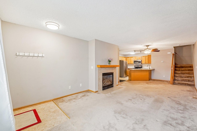 unfurnished living room with stairs, a textured ceiling, a tiled fireplace, and baseboards