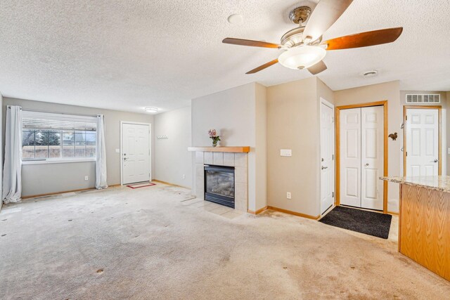 unfurnished living room with light colored carpet, visible vents, a tiled fireplace, a textured ceiling, and baseboards
