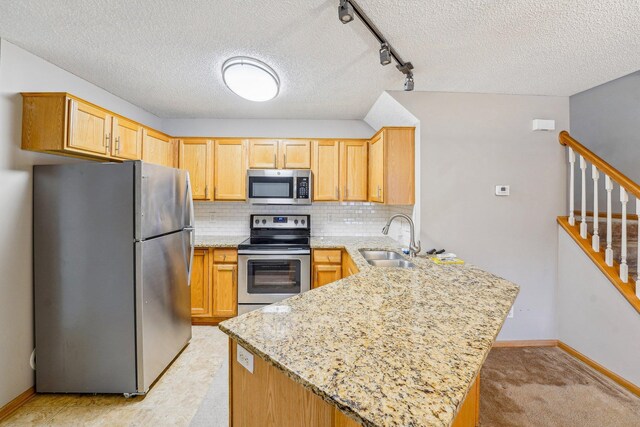 kitchen with a peninsula, light stone countertops, appliances with stainless steel finishes, and a sink