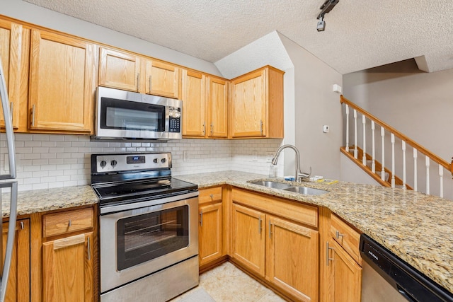 kitchen with a textured ceiling, a sink, appliances with stainless steel finishes, light stone countertops, and tasteful backsplash