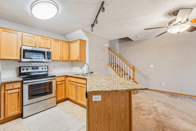 kitchen with a peninsula, a sink, appliances with stainless steel finishes, light stone countertops, and tasteful backsplash