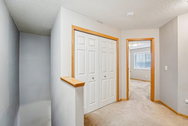 hall with light carpet, a textured ceiling, and baseboards