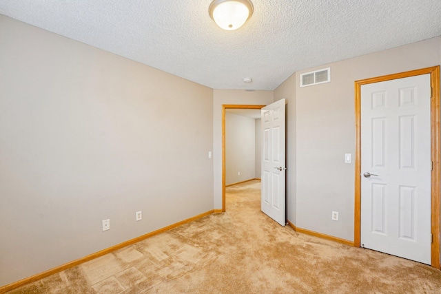 unfurnished bedroom with baseboards, a textured ceiling, visible vents, and light colored carpet