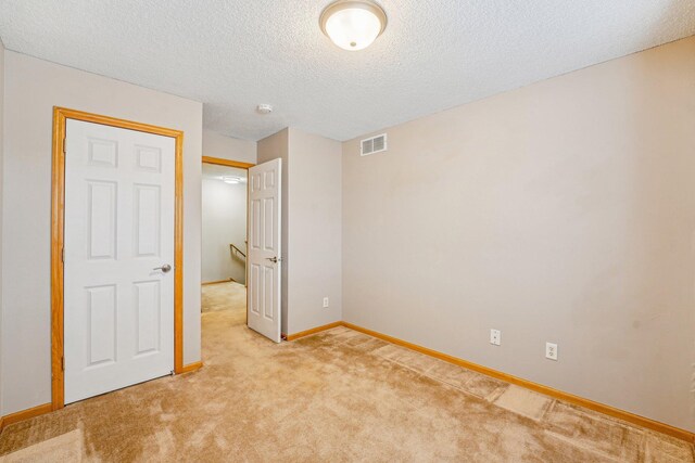 unfurnished bedroom with baseboards, visible vents, a textured ceiling, and light colored carpet