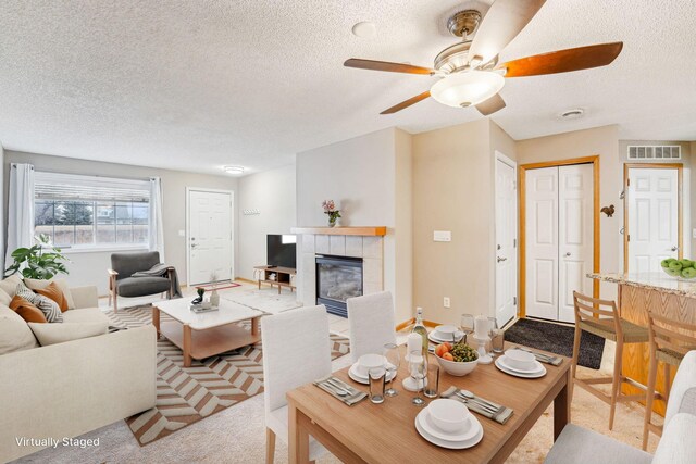 living room featuring light carpet, visible vents, a ceiling fan, a tiled fireplace, and a textured ceiling