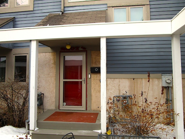 view of exterior entry with a shingled roof and stucco siding