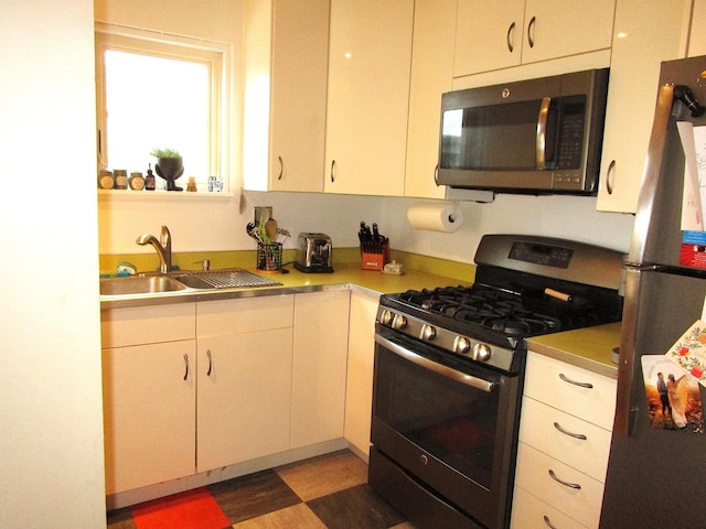 kitchen with appliances with stainless steel finishes, a sink, and white cabinetry