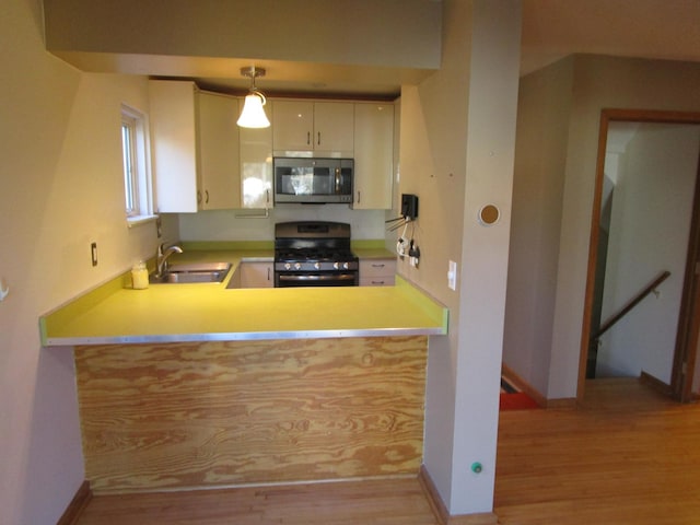 kitchen featuring a sink, baseboards, appliances with stainless steel finishes, light wood-type flooring, and pendant lighting