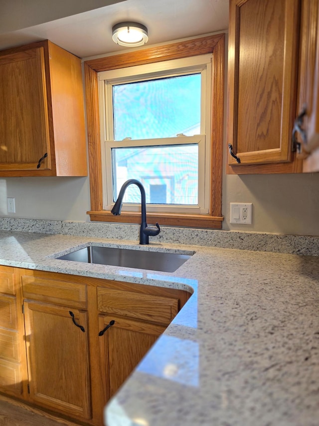 kitchen featuring brown cabinetry, light stone countertops, and a sink