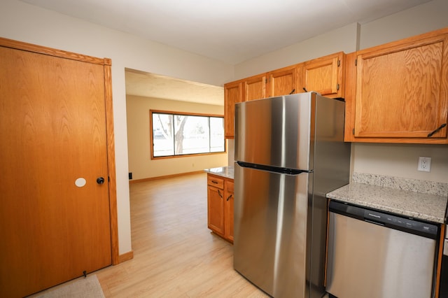 kitchen featuring baseboards, light stone counters, brown cabinets, light wood-style floors, and stainless steel appliances