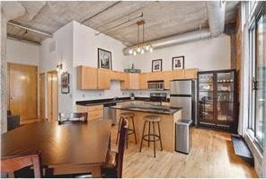 kitchen featuring pendant lighting, light hardwood / wood-style flooring, a towering ceiling, stainless steel appliances, and a notable chandelier