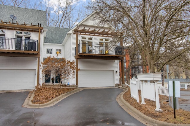 view of front of house with a balcony, an attached garage, driveway, and roof with shingles