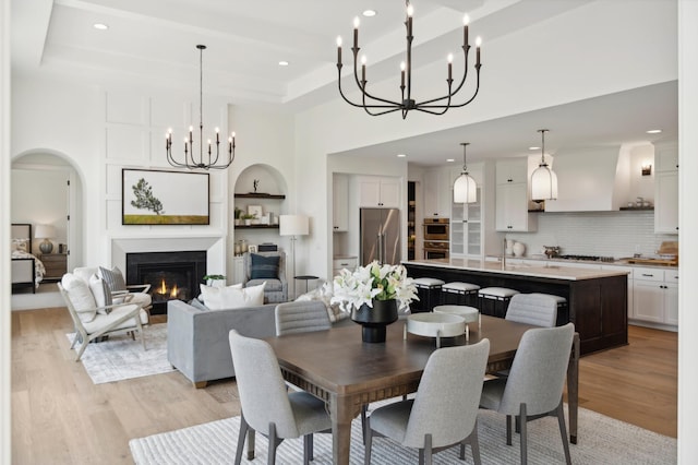 dining space with a towering ceiling, a tray ceiling, built in features, and light hardwood / wood-style flooring