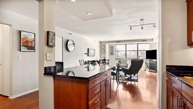 kitchen with reddish brown cabinets, dark countertops, wood finished floors, and baseboards