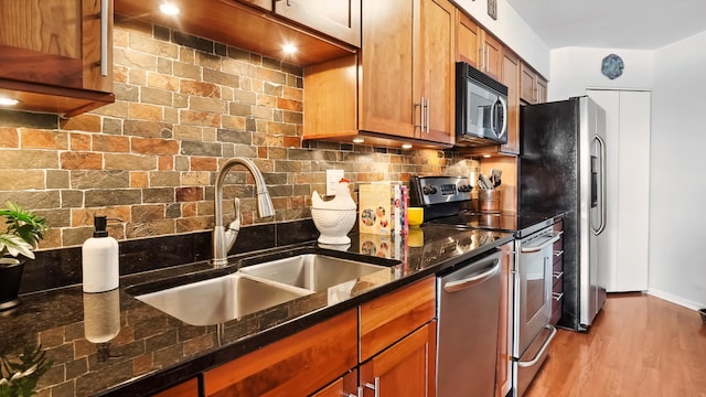 kitchen with dark stone counters, brown cabinets, a sink, stainless steel appliances, and backsplash