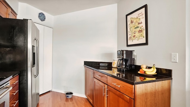 kitchen featuring baseboards, light wood-style floors, brown cabinets, dark stone countertops, and stainless steel fridge