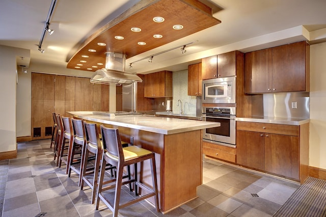 kitchen with stainless steel appliances, a spacious island, light countertops, brown cabinets, and a kitchen bar