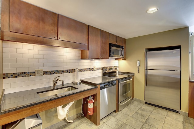 kitchen featuring stainless steel appliances, a sink, baseboards, backsplash, and dark stone countertops