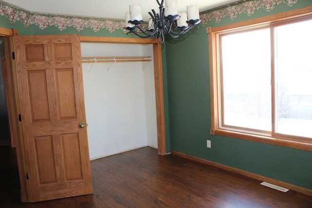 unfurnished bedroom featuring an inviting chandelier, a textured ceiling, dark hardwood / wood-style flooring, and a closet