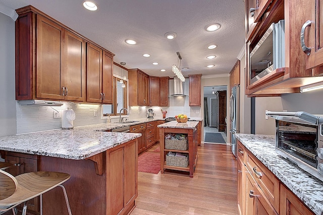 kitchen with stainless steel appliances, light stone countertops, light hardwood / wood-style floors, a kitchen bar, and wall chimney exhaust hood