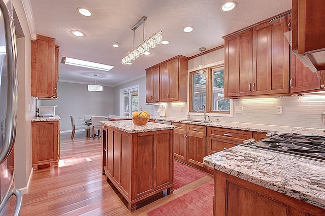 kitchen with sink, crown molding, light stone countertops, a kitchen island, and decorative light fixtures