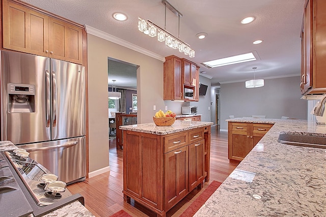 kitchen featuring appliances with stainless steel finishes, a skylight, hanging light fixtures, ornamental molding, and light stone counters