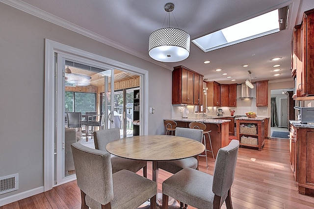 dining space with crown molding, sink, a skylight, and light hardwood / wood-style floors